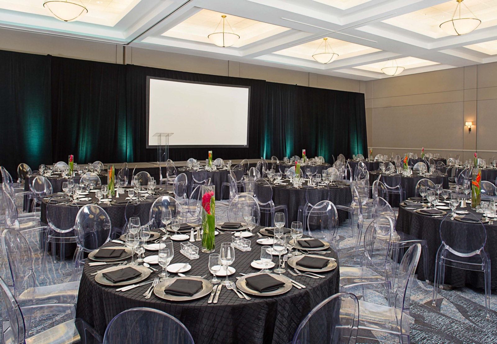 Evening reception set with dark linens, ghost chairs, and uplighting